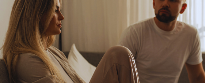 Couple sitting on a couch having a serious conversation with emotional distance and tension after broken trust