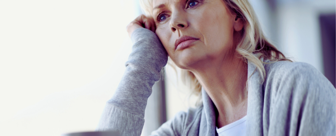 Woman sitting by a window looking thoughtful and emotionally tired, reflecting the strain of monitoring a loved one’s addiction recovery