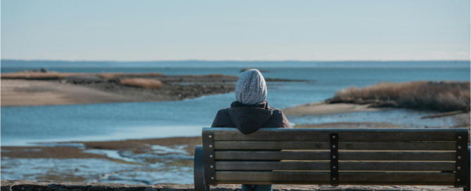 Person sitting alone on a bench overlooking water reflecting on emotional sobriety and personal growth after addiction recovery