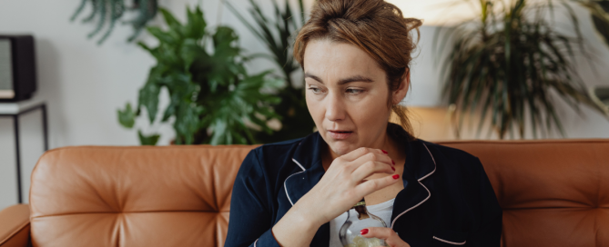 woman sitting at home holding a bottle looking uncertain about her drinking