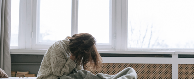 Person sitting on a bed in distress after discovering a partner’s sex or porn addiction